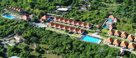 Vista aérea de un resort con varias cabañas, una piscina central y exuberante vegetación que rodea la propiedad.