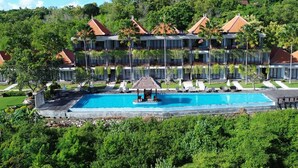 Un hôtel à plusieurs étages doté d’une piscine, entouré d’une végétation luxuriante et de palmiers.