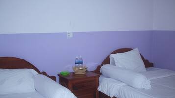 Une chambre d’hôtel avec deux lits simples, une table de chevet en bois avec un panier, et une prise électrique au mur.