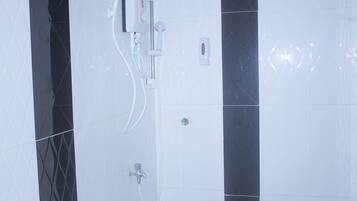 Un baño con ducha, secamanos y dispensador de jabón en la pared.