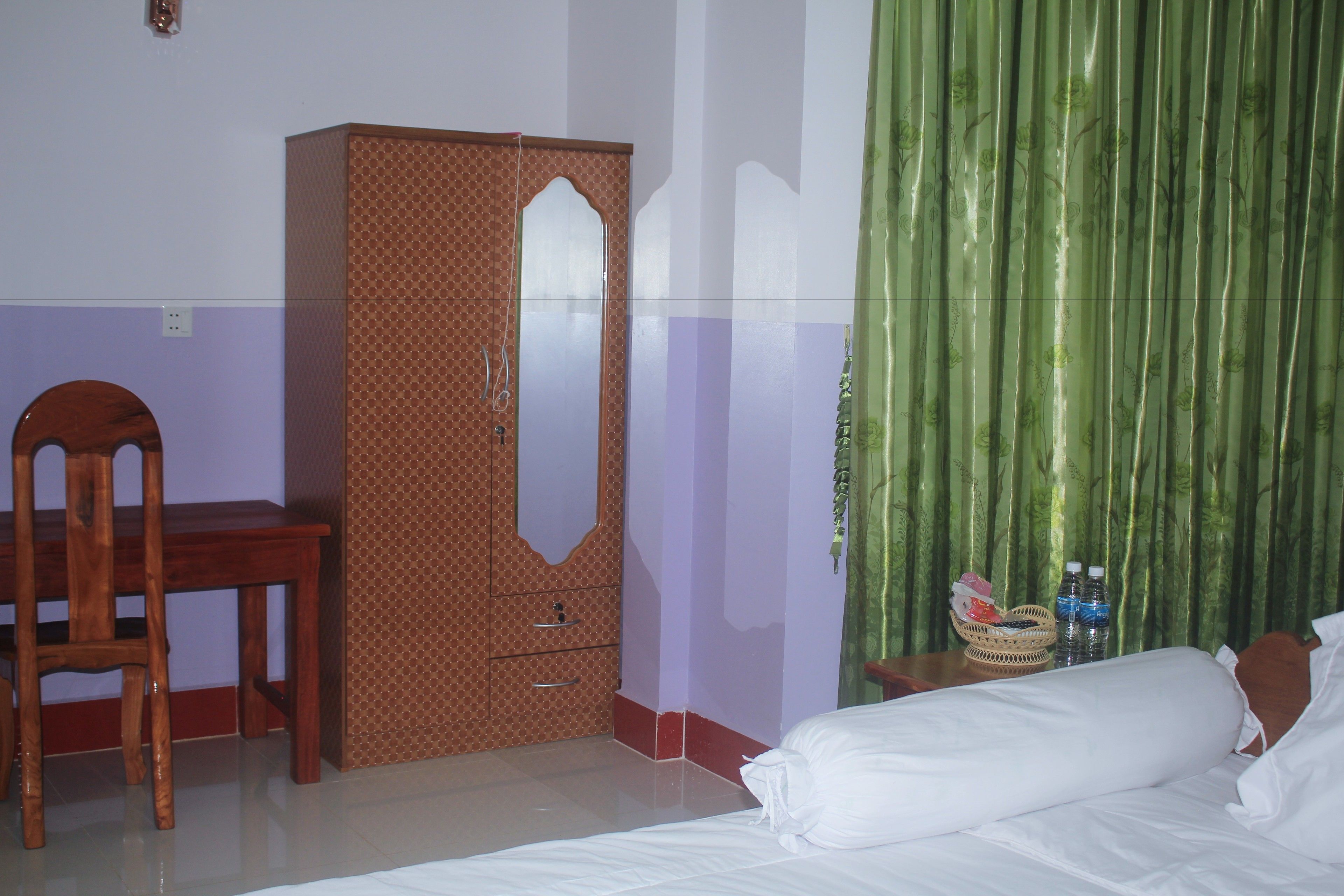 A bedroom with a bed, a wooden wardrobe, a chair, and a nightstand with water bottles.