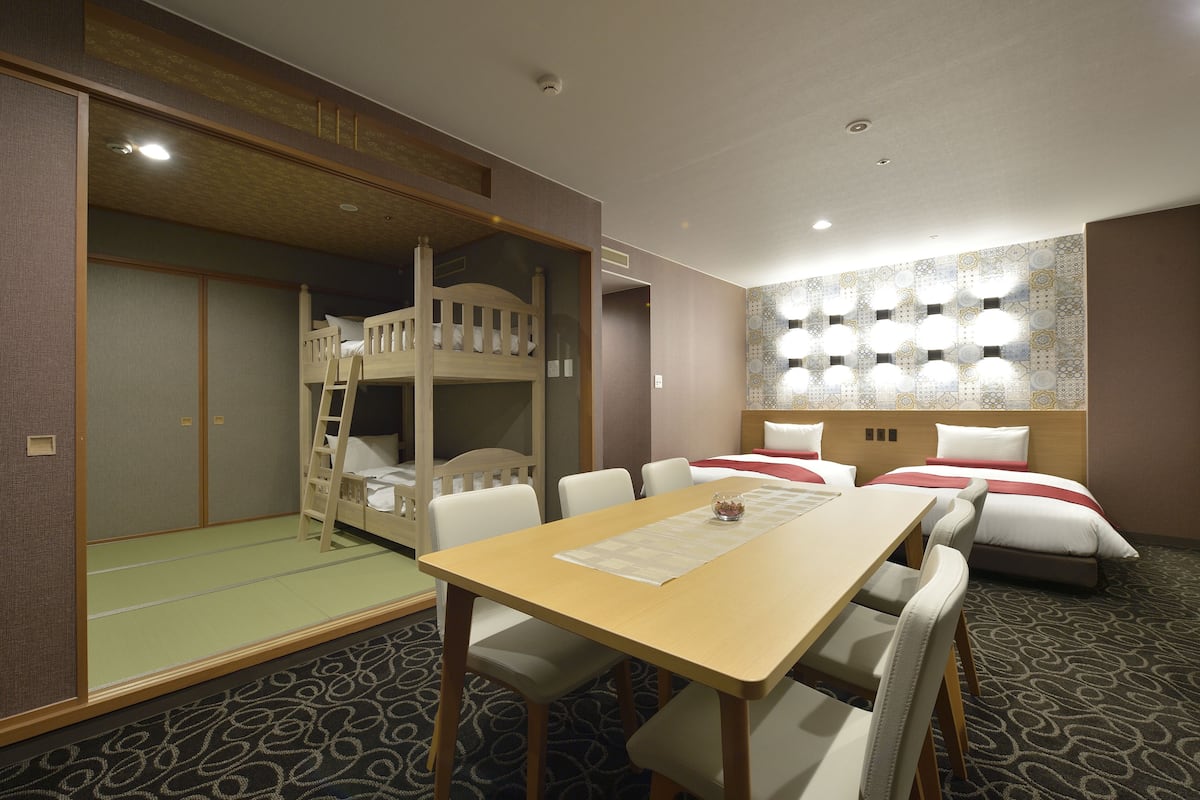 A hotel room with a bunk bed, a dining table, and a patterned carpet.