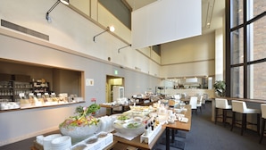 A spacious dining area with multiple tables and chairs, a buffet with various food items, and a large window providing natural light. - Hotel WBF Sapporo Odori (Sapporo)