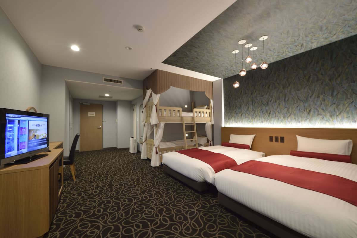 A hotel room with two beds, a TV, a desk, and a bathroom.
