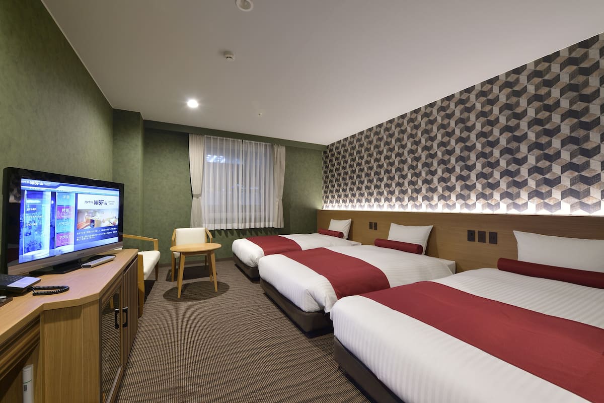 A hotel room with three beds, a desk with a computer, a television, and a window with curtains.