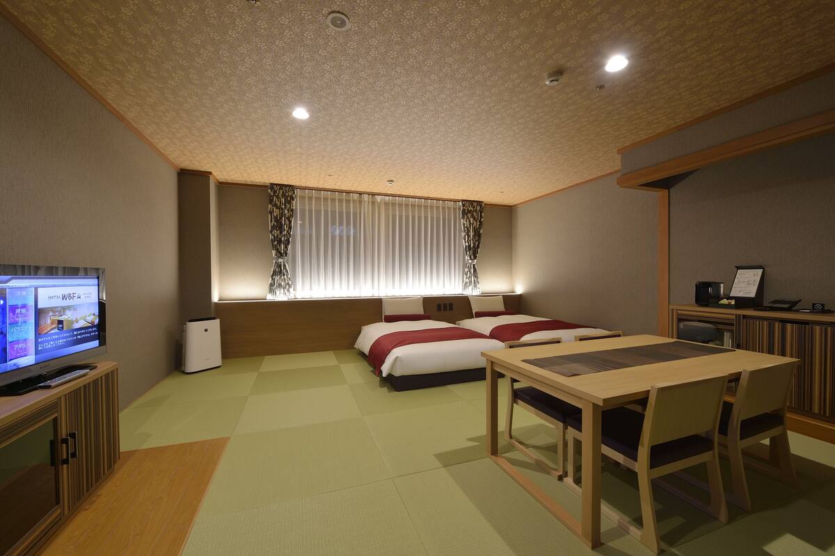 A hotel room with a TV, two beds, a desk, and a window with curtains.