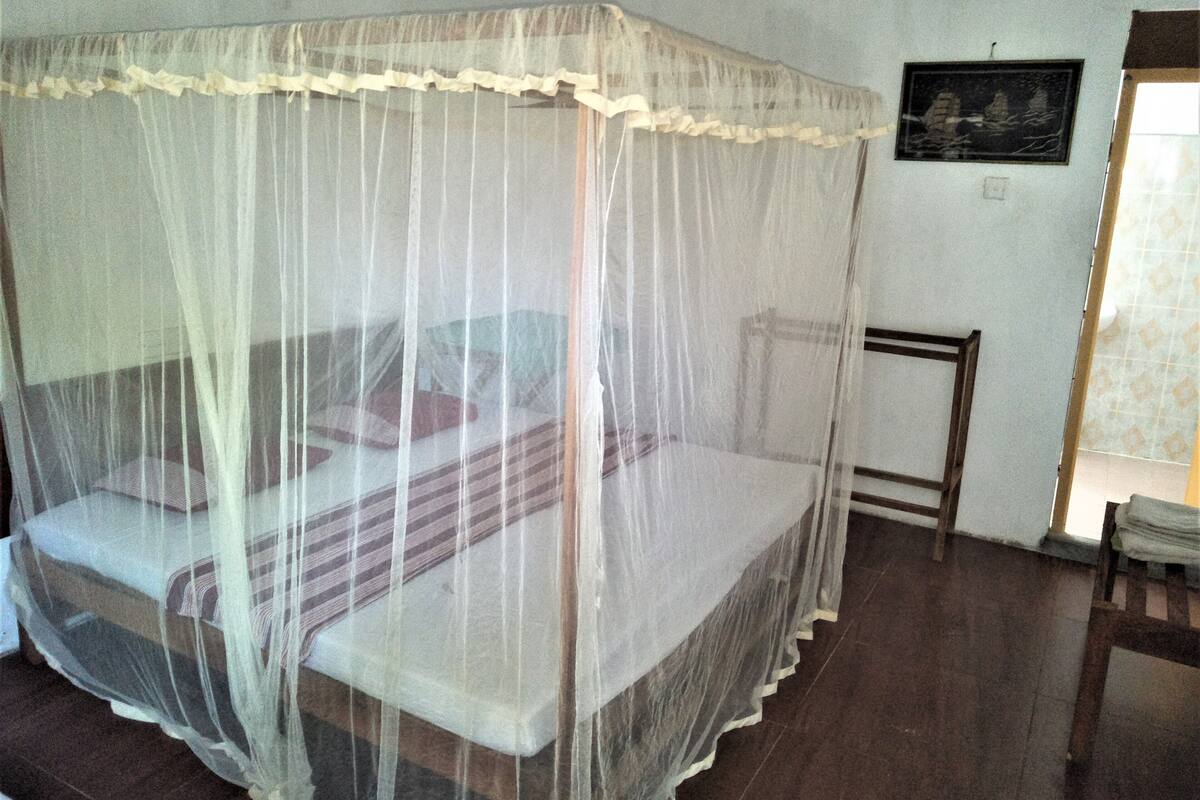 Una cama individual con mosquitera, cabecera de madera y una mesita de noche.