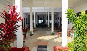 A spacious indoor area with high ceilings and columns, featuring several potted plants and wooden furniture. - Hansa Surf Hotel (Hikkaduwa)