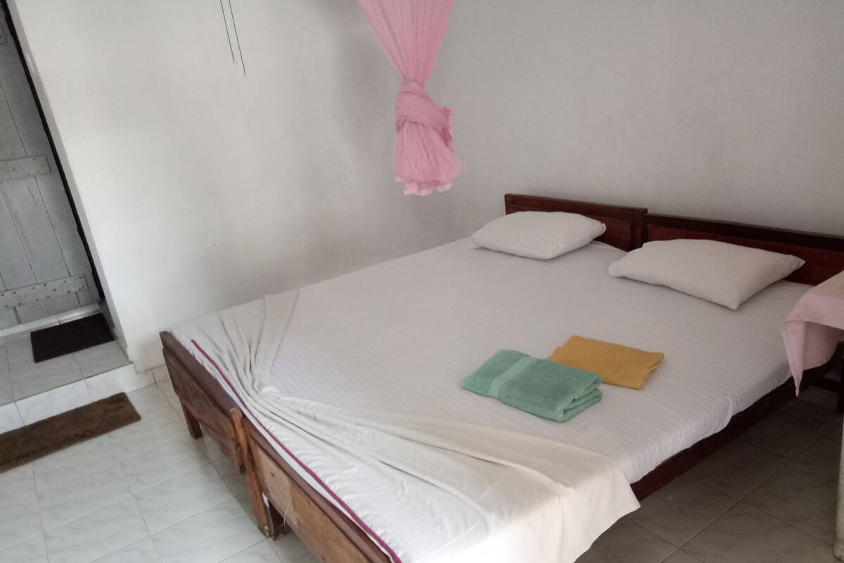 Una cama individual con ropa de cama blanca, dos almohadas y un dosel rosa.