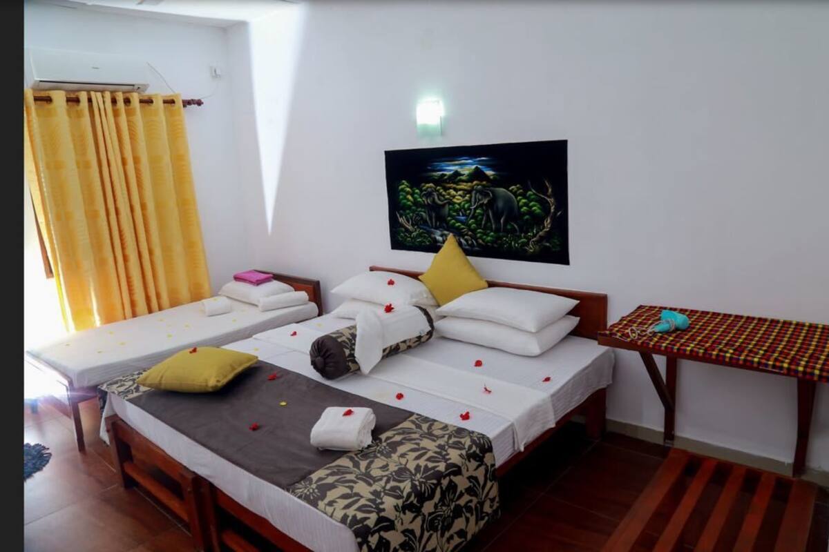 Una habitación con dos camas, una mesita, un cuadro en la pared y una ventana con cortinas.