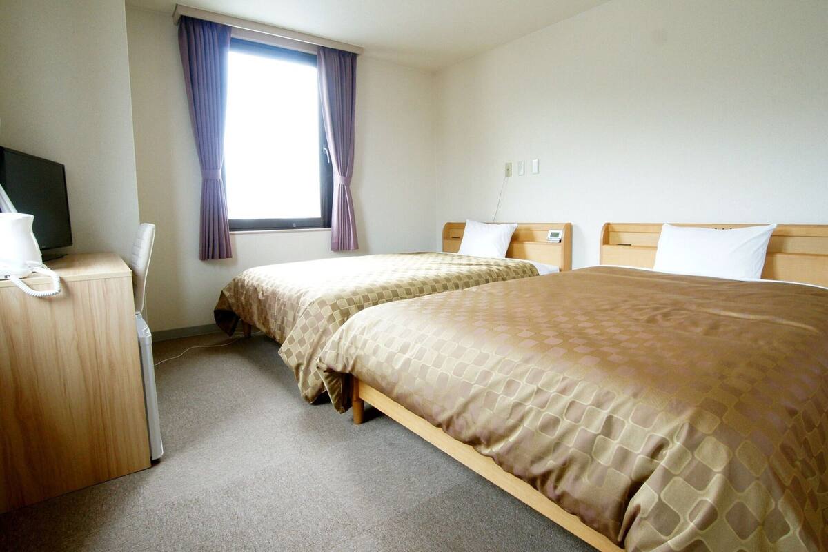 Een hotelkamer met twee bedden, een bureau met telefoon en een raam met gordijnen.