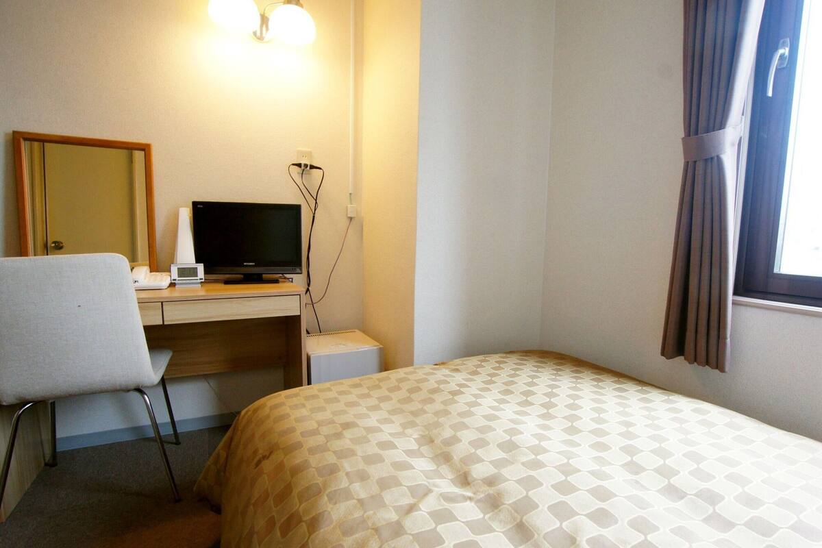 Een hotelkamer met een bed, een bureau met een computer, een stoel en een raam met gordijnen.