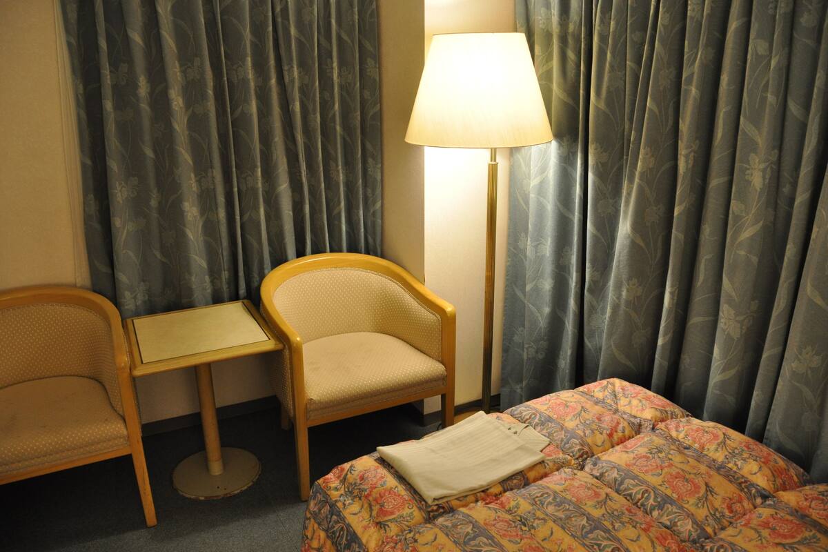 A hotel room with a bed, a chair, a small table, and a lamp.