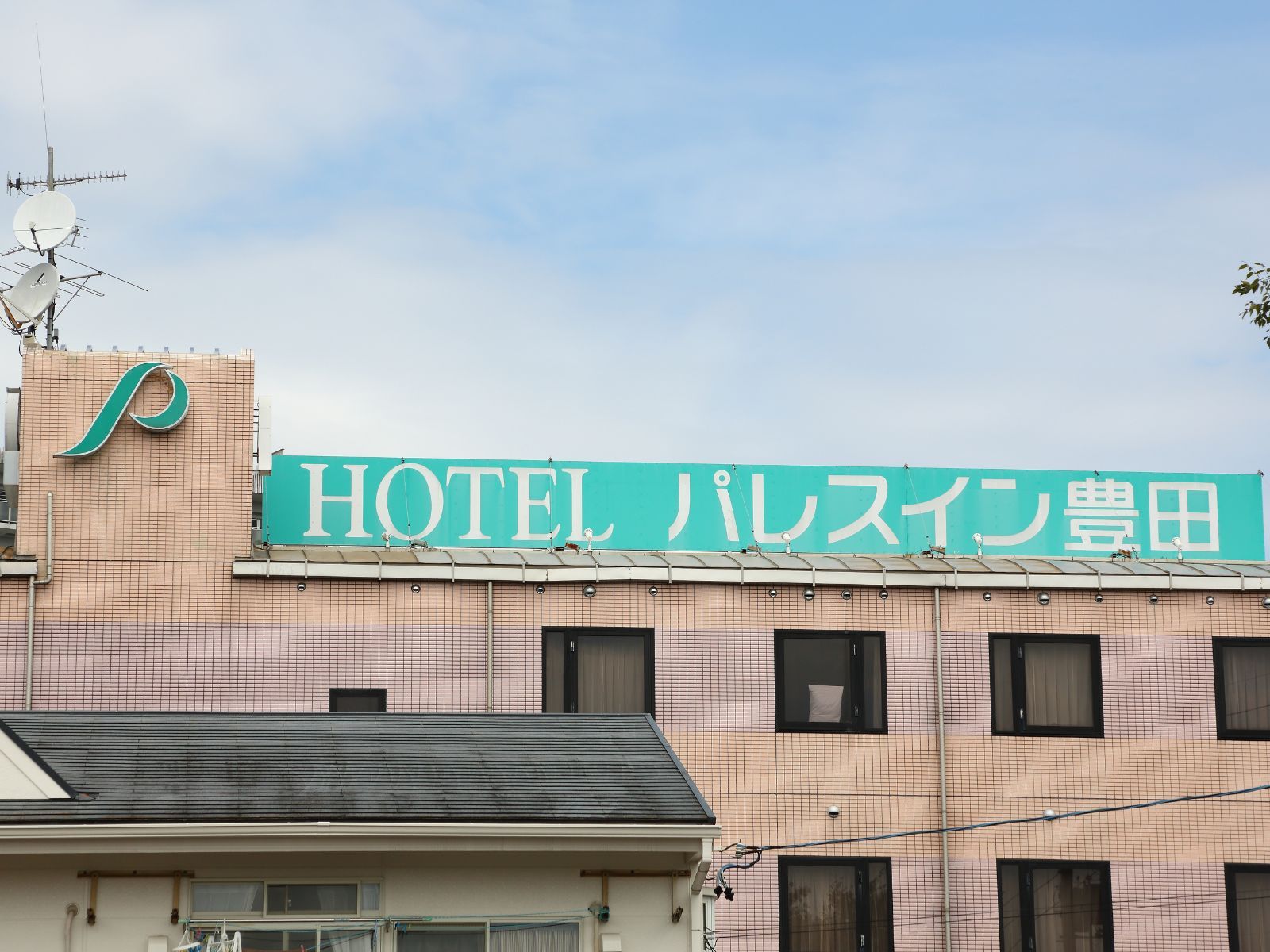 A hotel sign with Japanese characters, a tiled facade, and a satellite dish.