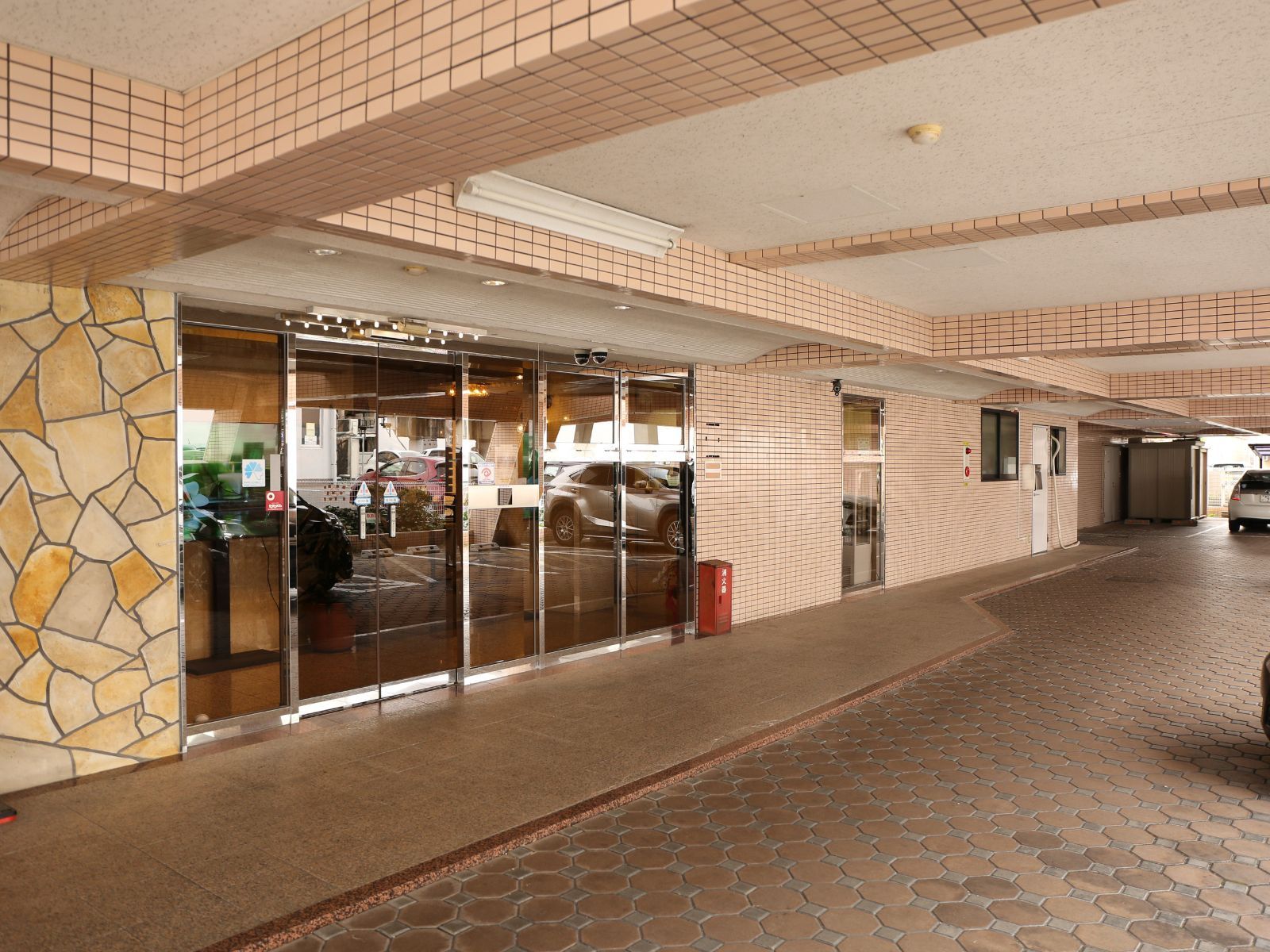 A building entrance with a tiled facade, a glass door entrance, and a paved walkway.