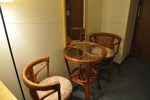 Um quarto com uma pequena mesa e quatro cadeiras de vime, uma porta e piso coberto de carpete.