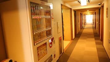Un couloir d’hôtel avec un distributeur automatique sur la gauche, des portes sur la droite et un sol recouvert de moquette.