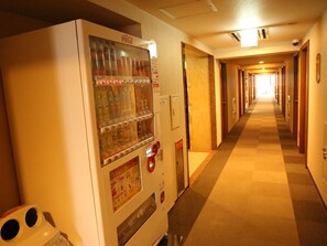 Pasillo de hotel con una máquina expendedora a la izquierda, puertas a la derecha y suelo alfombrado.