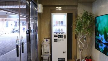 A vending machine with beverages and snacks, a trash bin, and a potted plant.