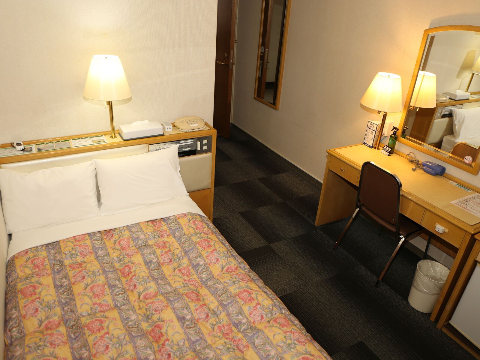 Habitación de hotel con cama, mesita de noche, escritorio, silla y espejo.