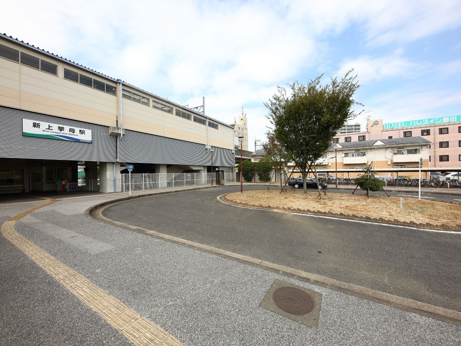 A building with a sign for Shin-Uwa Station, a parking area, and a tree.