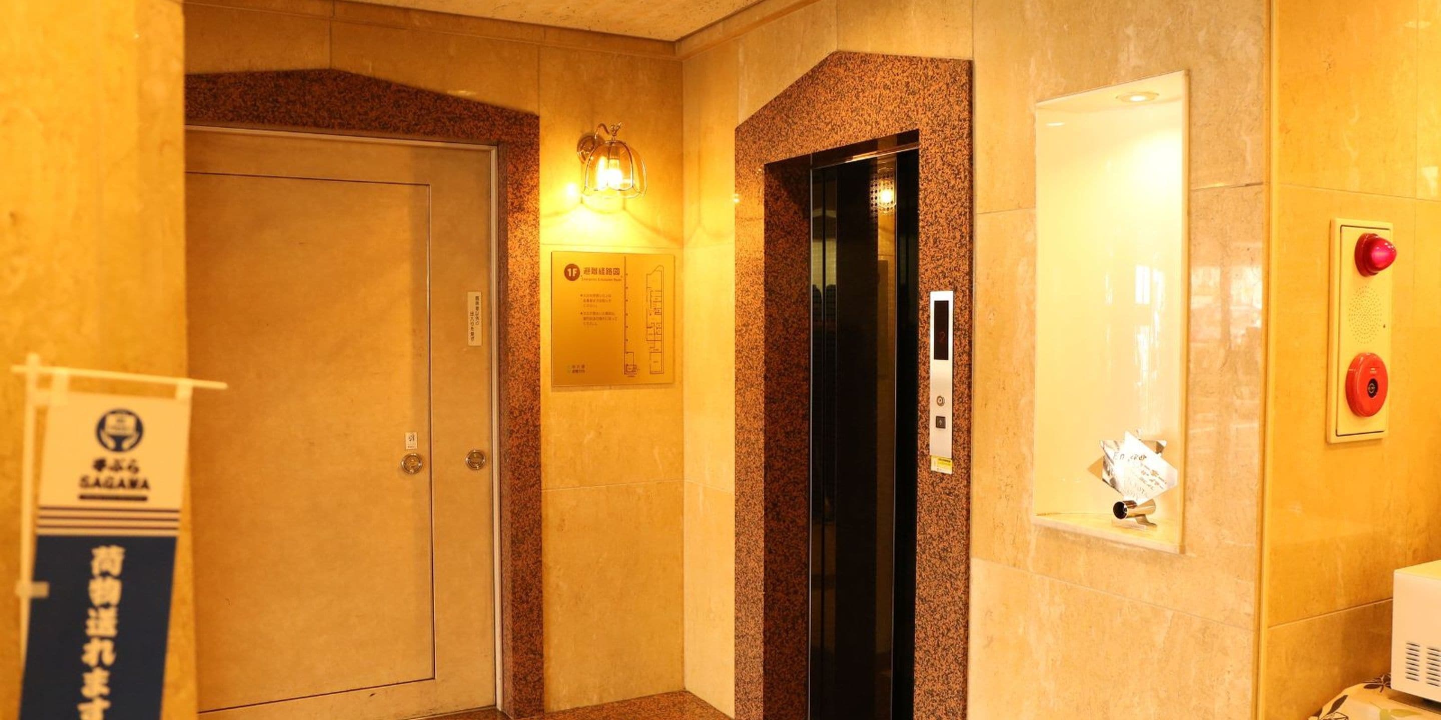 Interno di un ascensore con porta, plafoniera e pulsante di emergenza.