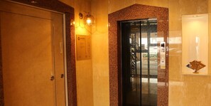 A hotel entrance with a closed door, a reception desk, and a glass elevator door. - Palace Inn Toyota (Toyota)