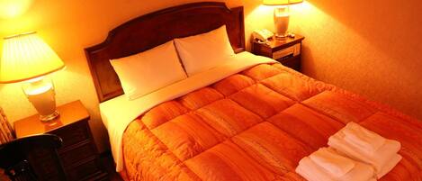 A hotel room with a large bed, two bedside lamps, a chair, and a small table with a lamp.