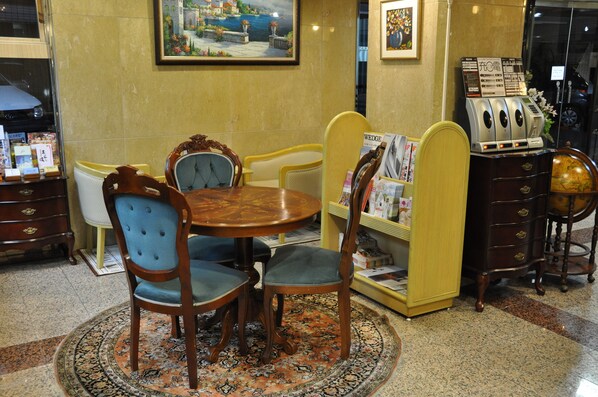 A hotel lobby with a round wooden table, blue upholstered chairs, a yellow armchair, a globe, and a magazine rack.