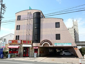Un hotel con fachada curva, entrada visible y estacionamiento con un automóvil.