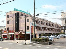 Um hotel com uma placa grande, várias janelas e estacionamento com carros.