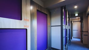 Un pasillo de hotel con puertas de vidrio de tono morado, puertas de habitaciones numeradas y suelo alfombrado.