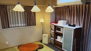 Un espacio habitable compacto con una mesa de comedor, cuatro taburetes, un microondas, un refrigerador pequeño y una lámpara.