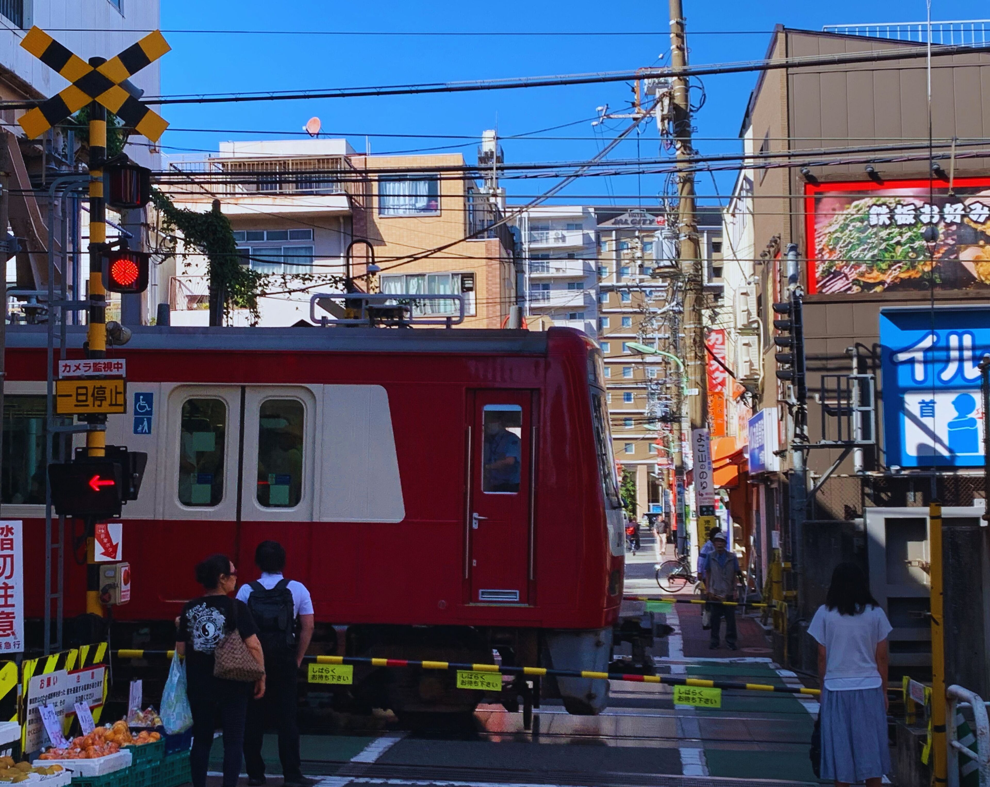 Un tranvía rojo en una concurrida intersección urbana, con edificios y tiendas al fondo.