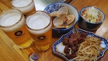Tres vasos de cerveza, un bol de almejas, un bol de verduras en vinagre y un plato de carne con fideos sobre una mesa de madera.