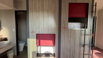A modern bathroom with a sink, toilet, and two bunk beds with red cushions.