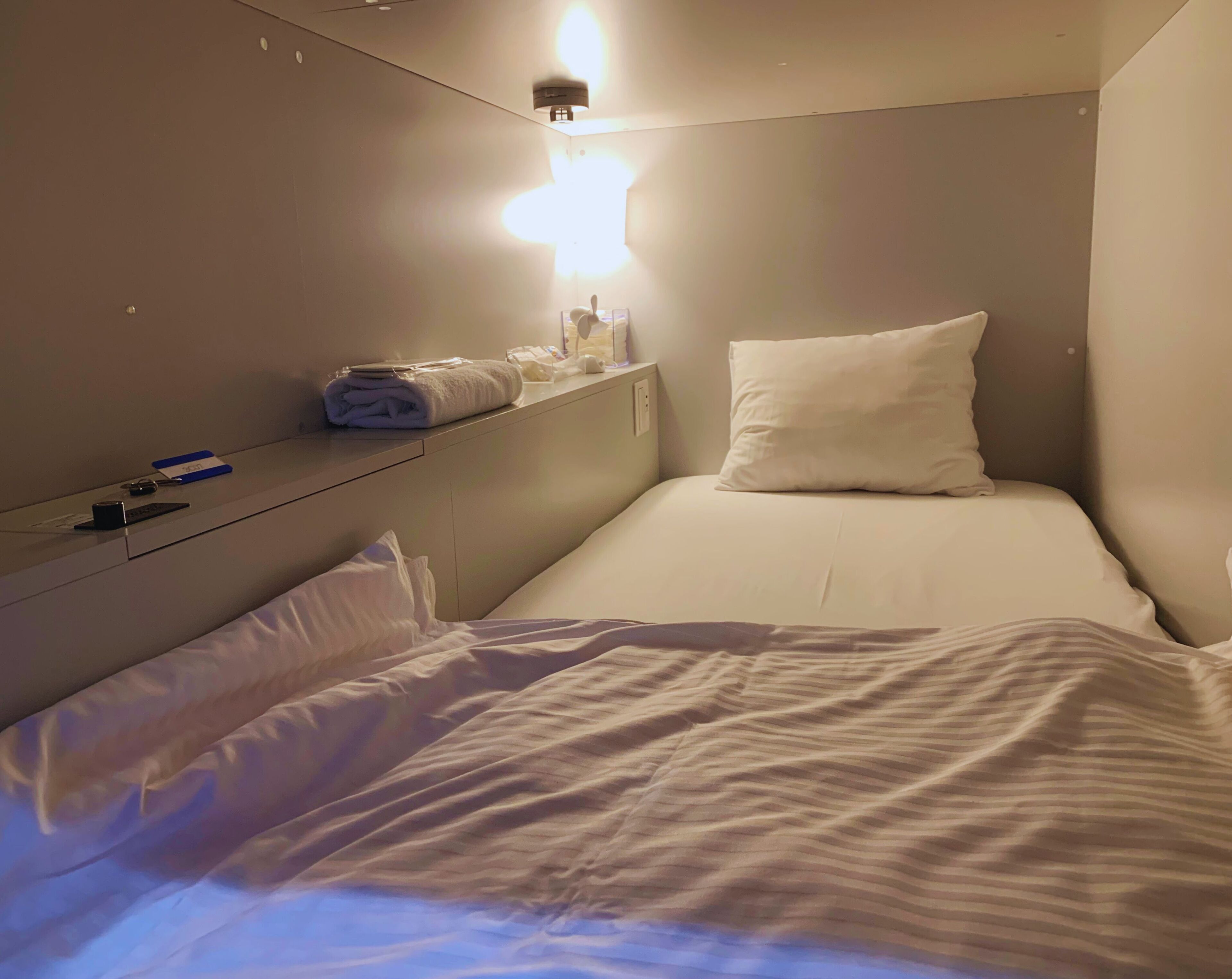 Una habitación pequeña con una cama individual, una mesita de noche, una lámpara de pared y una ventana.