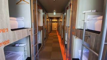 A hotel corridor with bunk beds labeled A23 and A22, a checkered floor, and a hallway leading to an exit.