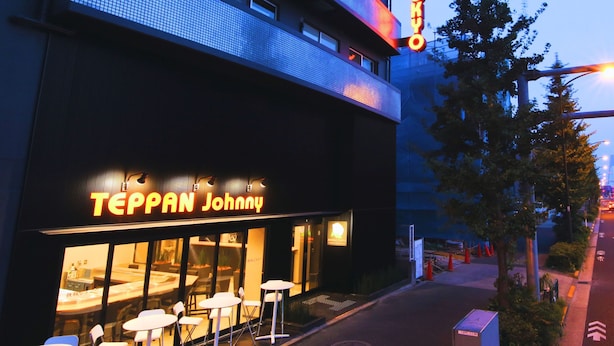 Un edificio con un letrero de neón que dice "TEPPAN Johnny" y un cartel encima que dice "BENJAMIN TOKYO".