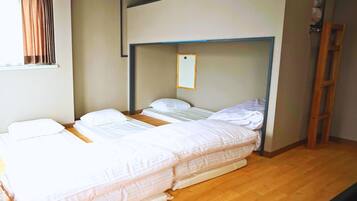 A room with two beds, wooden flooring, a window with curtains, and a wooden ladder.