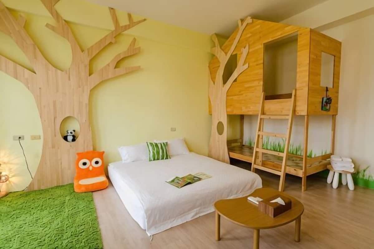 A bedroom with a bed, a wooden tree structure, a small table, and a green rug.