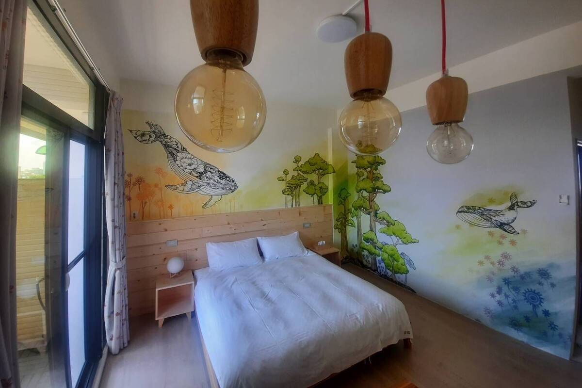 A bedroom with a wooden headboard, a bed with white bedding, and a mural of a whale and trees on the wall.