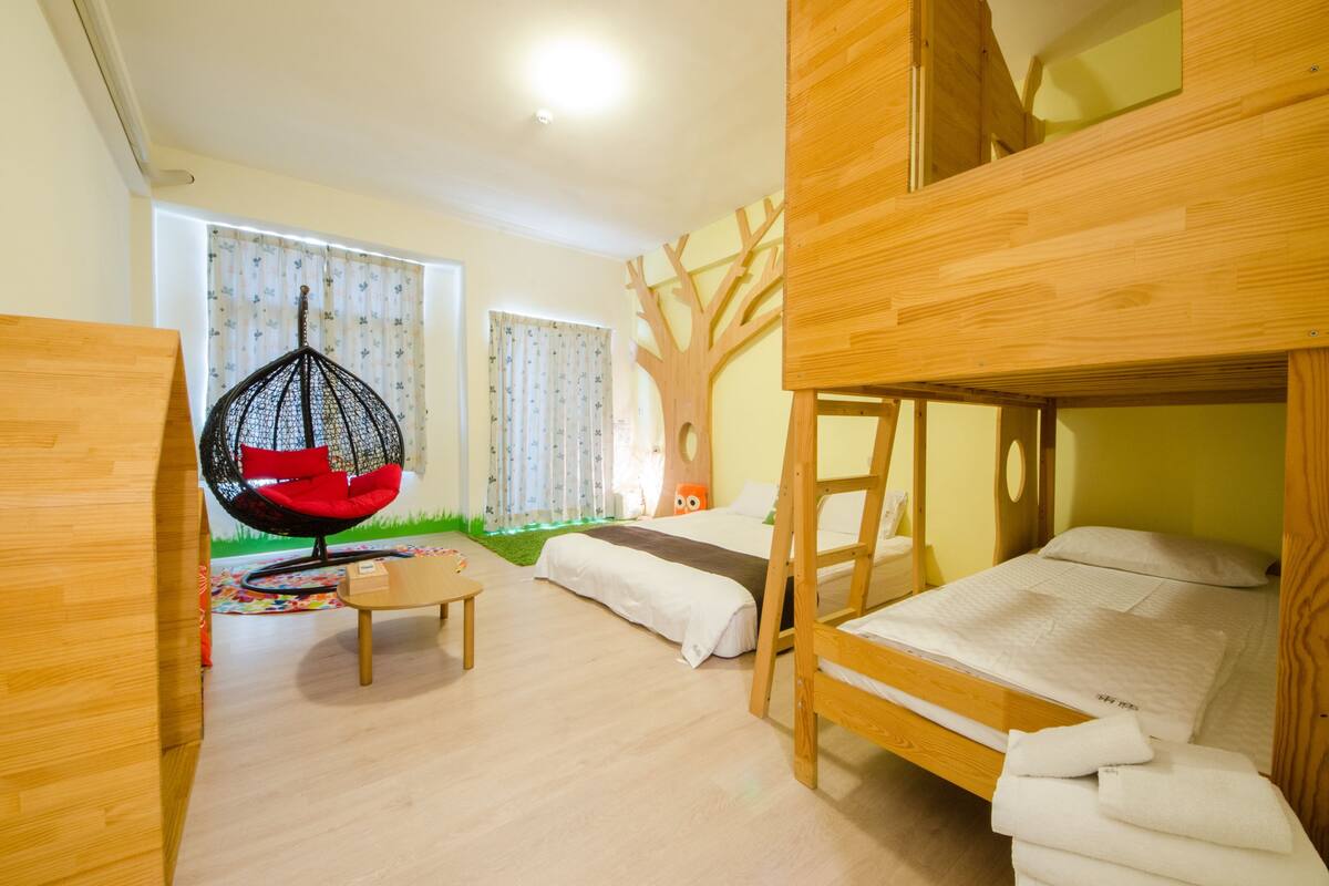 A children's room with bunk beds, a hanging chair, and a tree-shaped wall decoration.