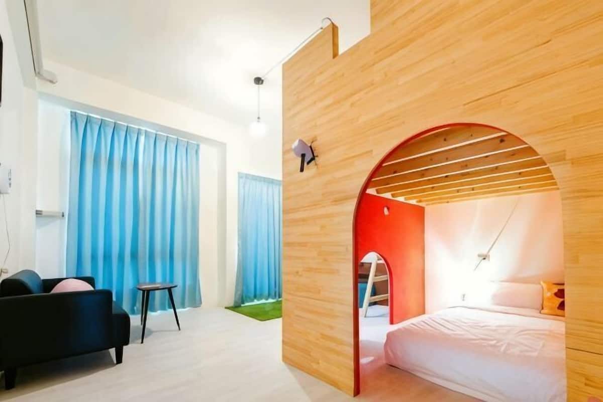 A modern bedroom with a wooden archway, a bed, a small seating area, and a window with curtains.