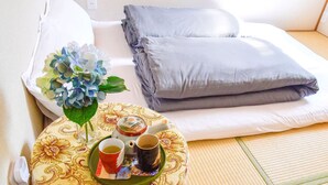 A neatly made bed with pillows and a tray with a teapot, cups, and a floral arrangement. - Guesthouse Hakuka - Hostel (Kanazawa)