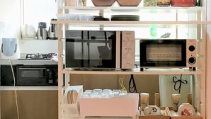 A kitchen with two microwaves, a gas stove, and various kitchen utensils on shelves. - Guesthouse Hakuka - Hostel (Kanazawa)