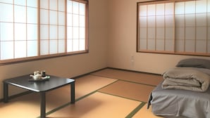 A room with tatami flooring, a futon bed, a low table with a teapot and cups, and large shoji screens. - Guesthouse Hakuka - Hostel (Kanazawa)