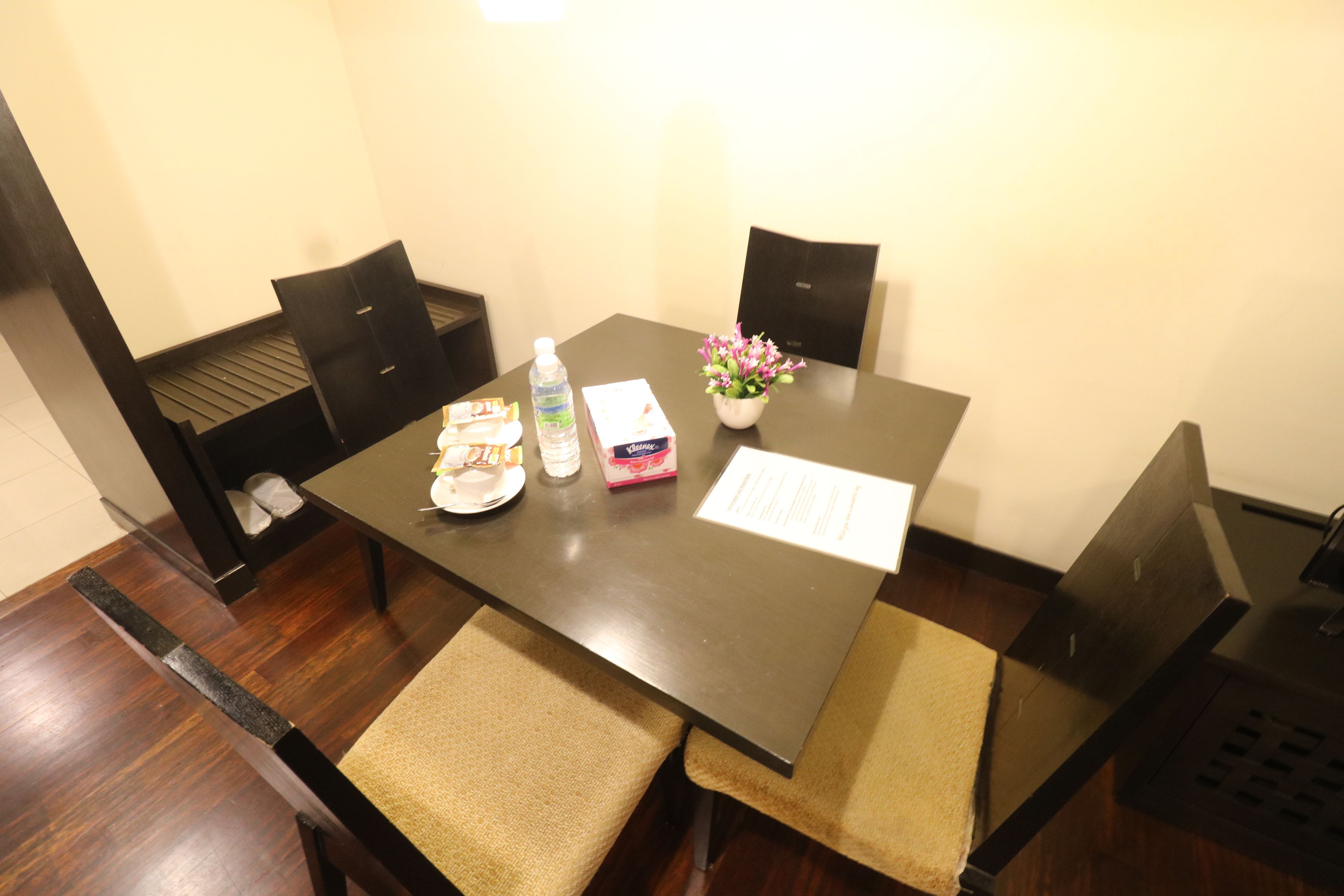A dining table with a placemat, a bottle of water, a box of tissues, a small vase with flowers, and a menu.