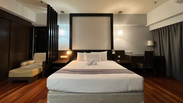 A hotel room with a large bed, a desk, a chair, and a sofa. - Raintree Resort suites at Bandar Sunway (Petaling Jaya)