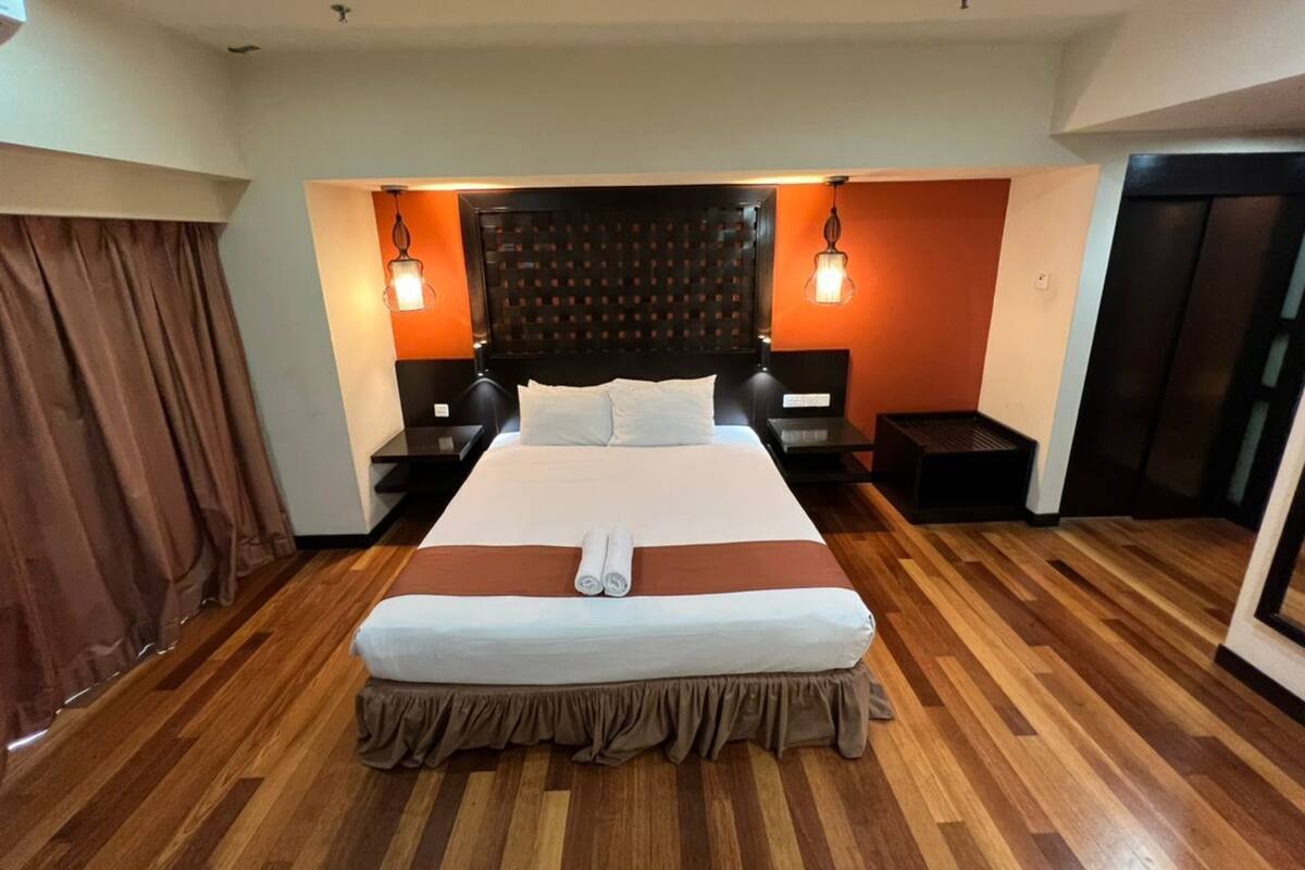 Une chambre d’hôtel avec un grand lit, un parquet en bois, deux tables de chevet et une tête de lit ornée d’un motif à carreaux.
